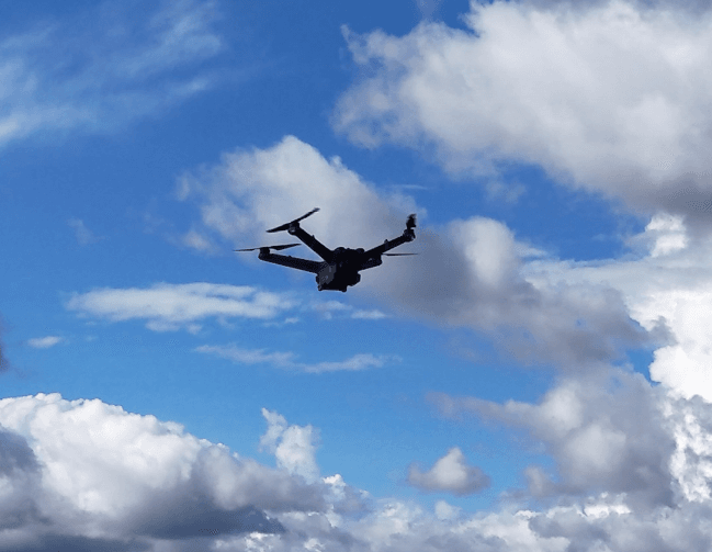 Drone nero in volo contro cielo azzurro nuvoloso